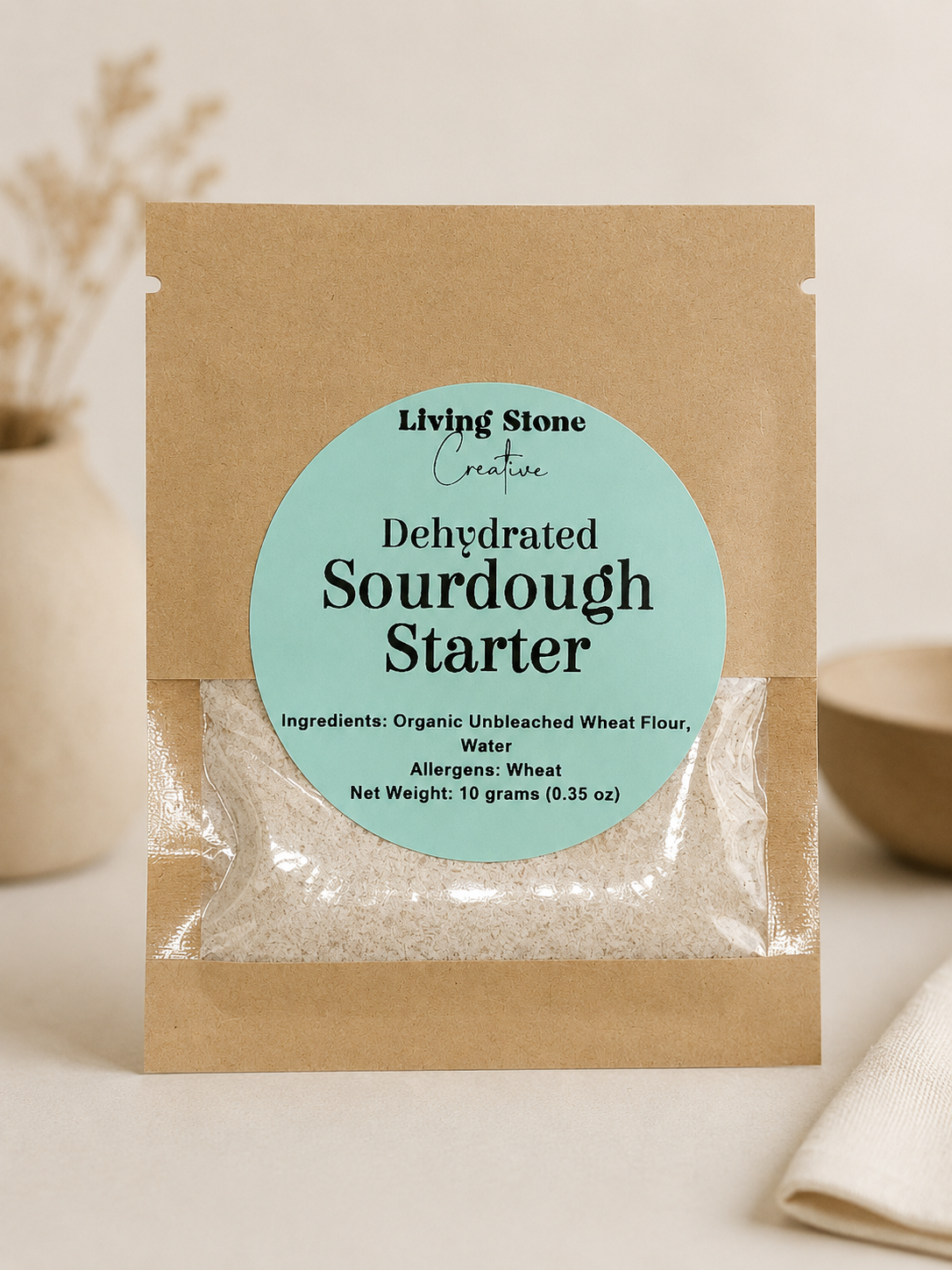 Kraft paper pouch of dehydrated sourdough starter with a pastel blue label and clear window showing dried starter flakes.