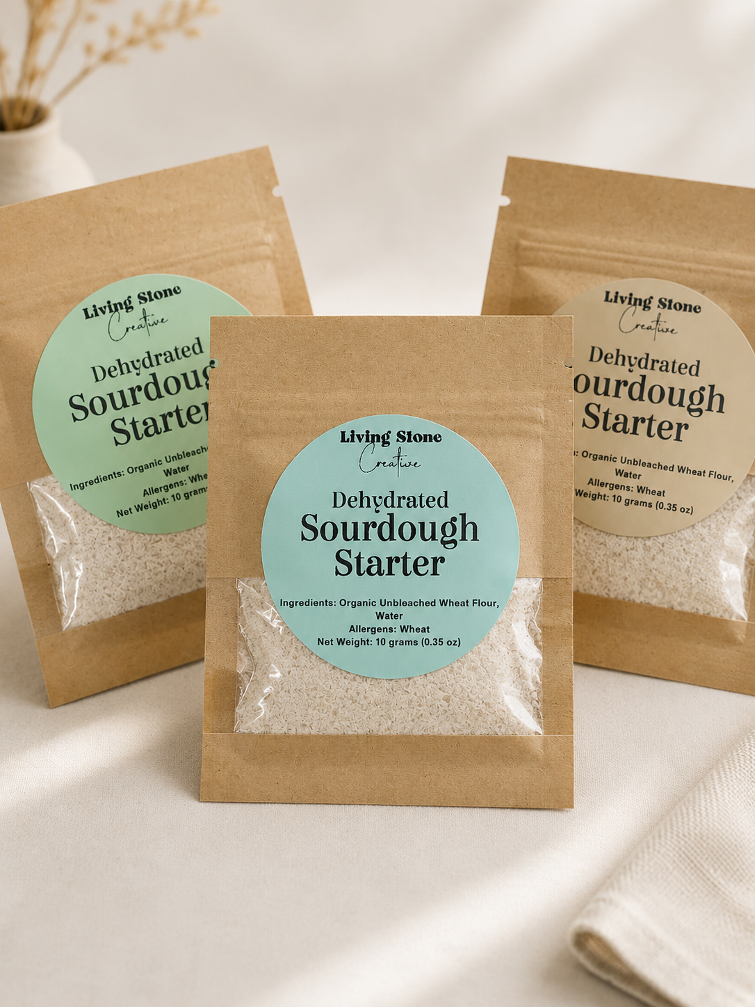3 Kraft paper pouches of dehydrated sourdough starter with a pastel blue label and clear window showing dried starter flakes.
